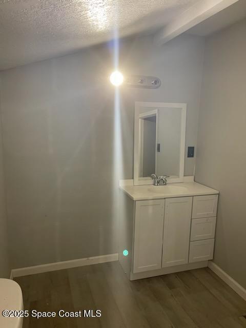 bathroom with hardwood / wood-style floors, vanity, vaulted ceiling with beams, toilet, and a textured ceiling