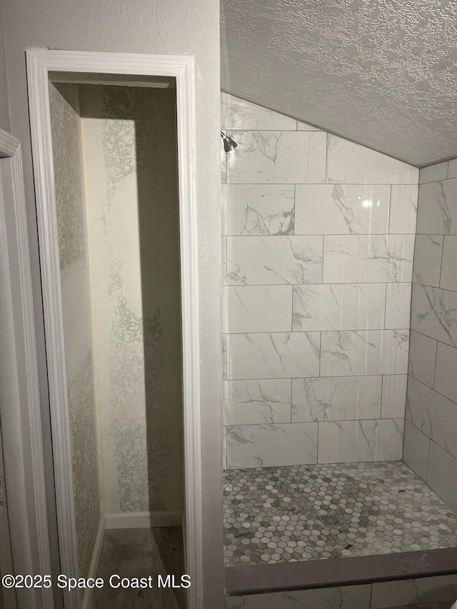 bathroom with a tile shower and lofted ceiling