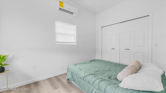 bedroom with a closet, an AC wall unit, and light hardwood / wood-style flooring