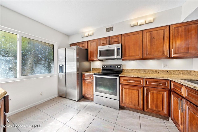 kitchen with light tile patterned floors, stainless steel appliances, light stone counters, and a healthy amount of sunlight