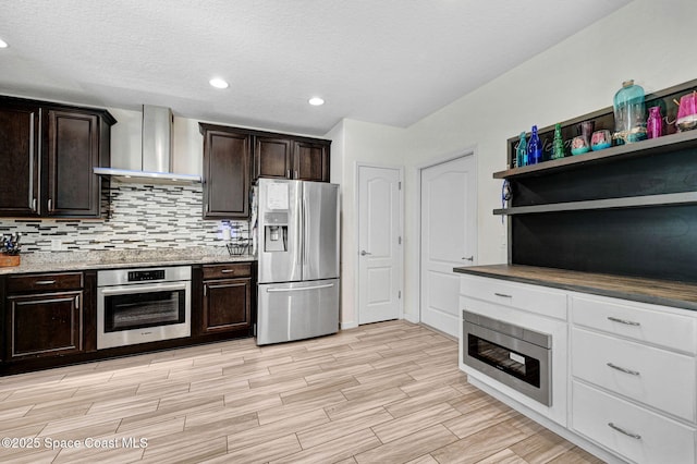 kitchen with wall chimney range hood, decorative backsplash, dark brown cabinetry, appliances with stainless steel finishes, and a textured ceiling