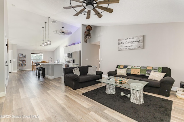 living room with light hardwood / wood-style floors, vaulted ceiling, ceiling fan, and sink