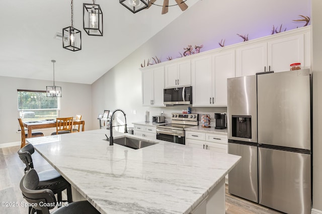 kitchen with appliances with stainless steel finishes, a kitchen island with sink, sink, pendant lighting, and white cabinets