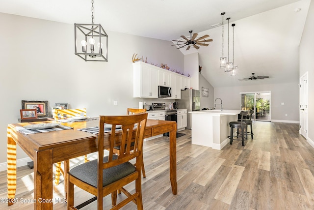 dining room with ceiling fan with notable chandelier, light hardwood / wood-style floors, high vaulted ceiling, and sink