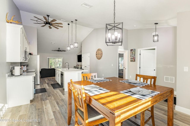 dining room with ceiling fan with notable chandelier, light wood-type flooring, and high vaulted ceiling