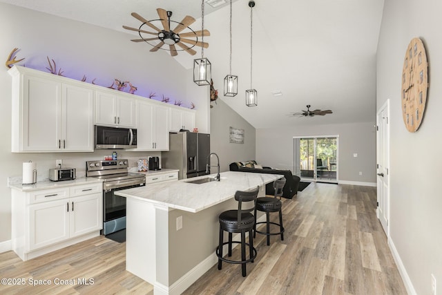 kitchen featuring appliances with stainless steel finishes, sink, a center island with sink, decorative light fixtures, and white cabinetry