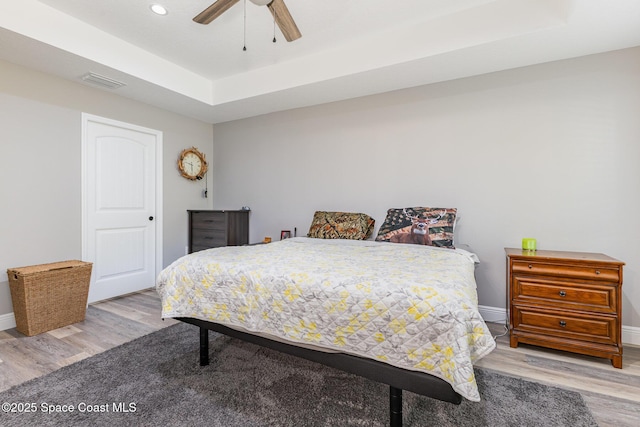 bedroom with light wood-type flooring, a tray ceiling, and ceiling fan