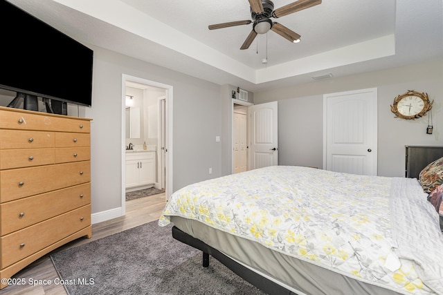 bedroom featuring a raised ceiling, ceiling fan, hardwood / wood-style floors, connected bathroom, and a closet