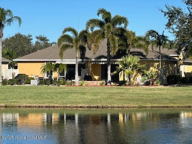 back of property with a water view and a lawn