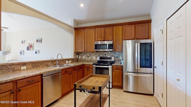 kitchen featuring light stone countertops, sink, stainless steel appliances, light hardwood / wood-style flooring, and backsplash