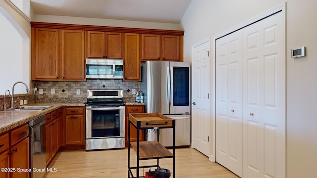 kitchen with light stone countertops, sink, light hardwood / wood-style floors, decorative backsplash, and appliances with stainless steel finishes