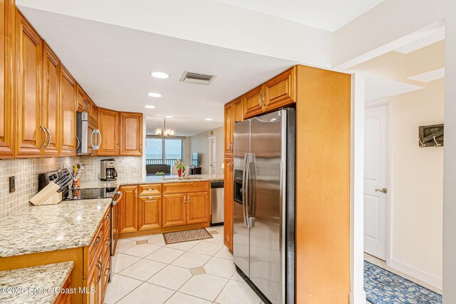 kitchen with backsplash, light stone countertops, light tile patterned floors, appliances with stainless steel finishes, and a chandelier