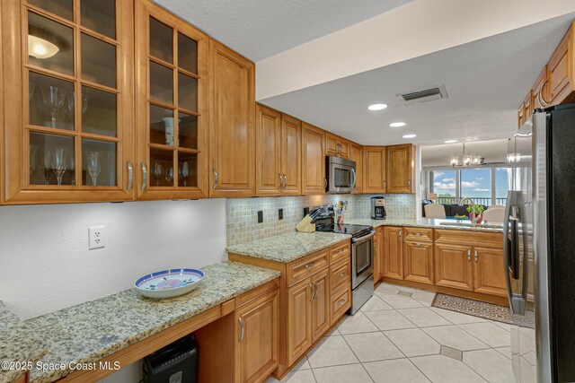 kitchen with light stone countertops, appliances with stainless steel finishes, backsplash, light tile patterned floors, and an inviting chandelier