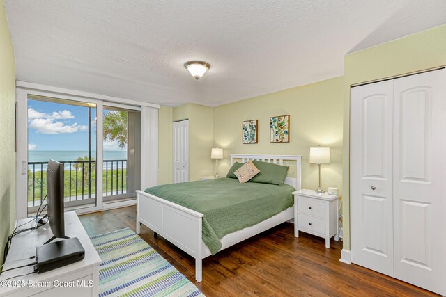 bedroom featuring dark hardwood / wood-style flooring, access to exterior, a textured ceiling, and two closets