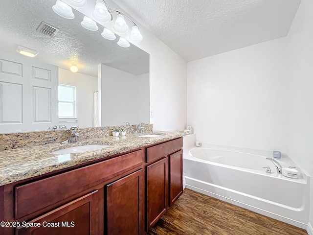 bathroom with a tub to relax in, vanity, wood-type flooring, and a textured ceiling