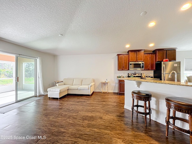 kitchen with a kitchen bar, appliances with stainless steel finishes, a textured ceiling, and light stone counters