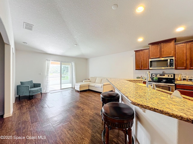 kitchen featuring light stone countertops, appliances with stainless steel finishes, dark hardwood / wood-style flooring, a textured ceiling, and a breakfast bar area