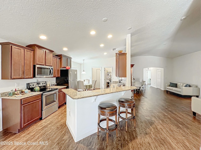 kitchen featuring stainless steel appliances, light stone counters, a textured ceiling, vaulted ceiling, and a breakfast bar area