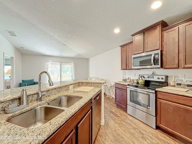 kitchen featuring light stone countertops, sink, light hardwood / wood-style floors, a textured ceiling, and appliances with stainless steel finishes