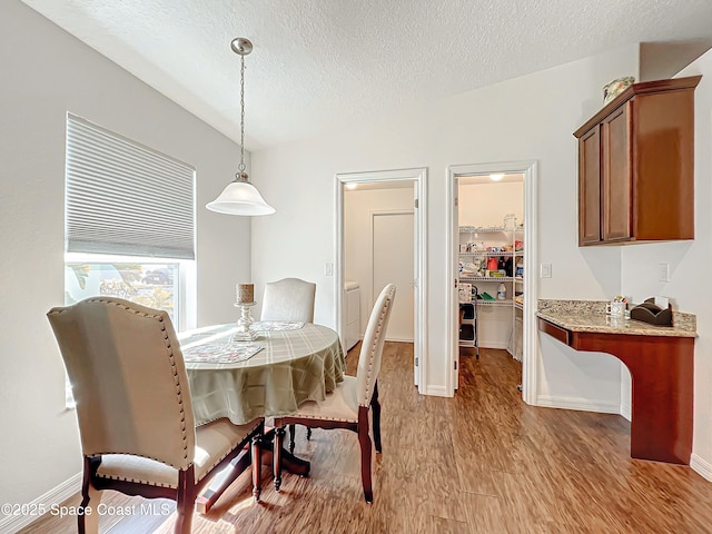 dining space with a textured ceiling, light hardwood / wood-style flooring, and lofted ceiling