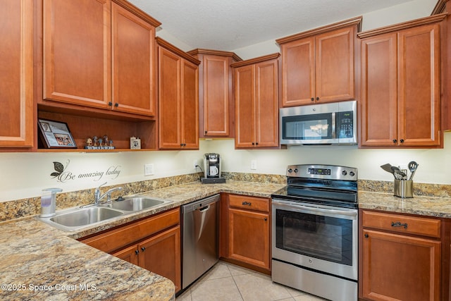 kitchen featuring light stone counters, sink, light tile patterned floors, and stainless steel appliances