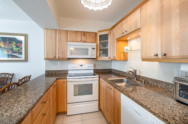 kitchen featuring dark stone countertops, sink, light tile patterned floors, and white appliances