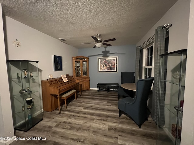 living area with ceiling fan, wood-type flooring, and a textured ceiling