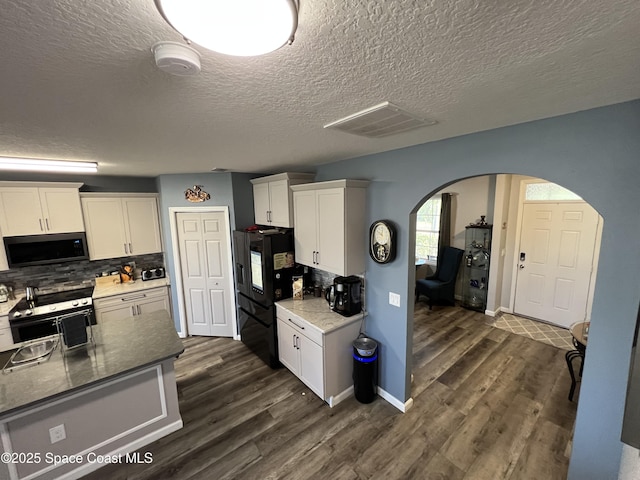 kitchen with stainless steel range with electric stovetop, backsplash, black fridge, dark hardwood / wood-style floors, and white cabinetry