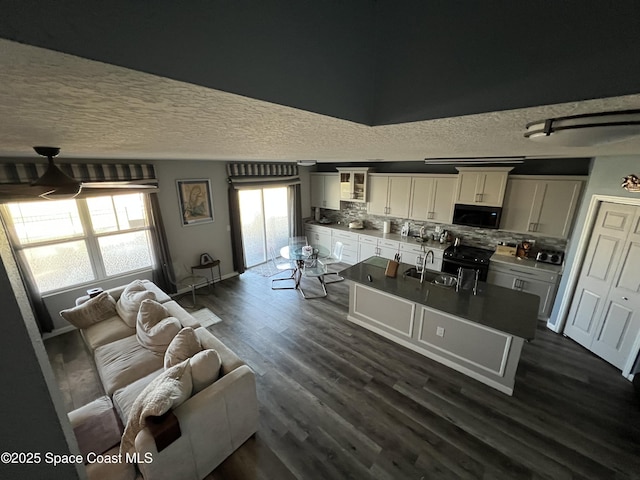 kitchen featuring tasteful backsplash, dark wood-type flooring, sink, black appliances, and a center island with sink