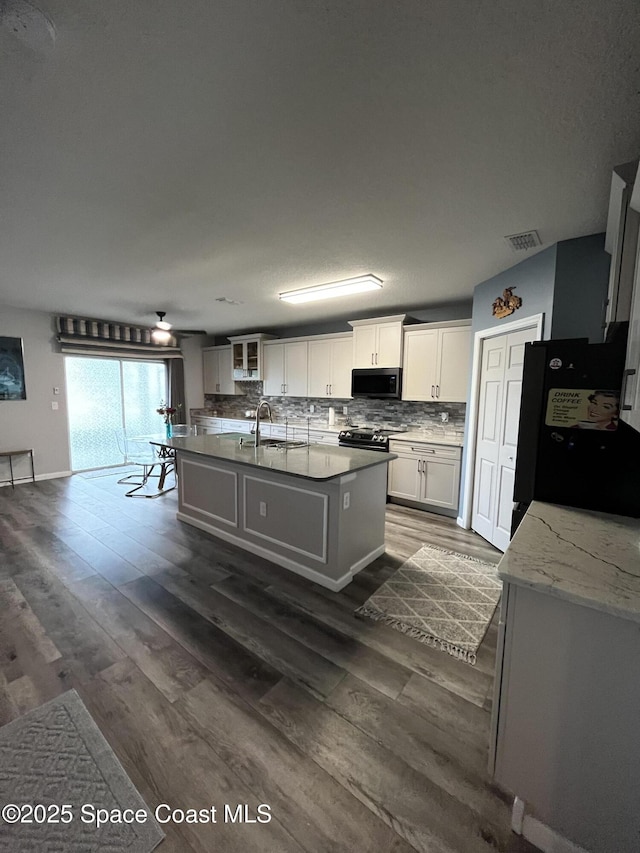 kitchen featuring sink, dark hardwood / wood-style floors, a kitchen island with sink, white cabinets, and black appliances