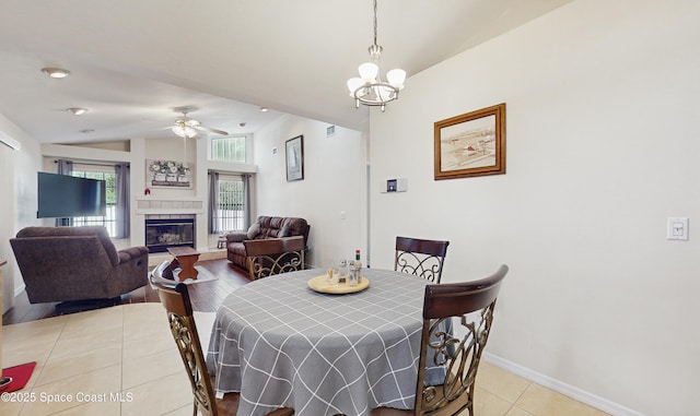 tiled dining room with a fireplace, ceiling fan with notable chandelier, and lofted ceiling