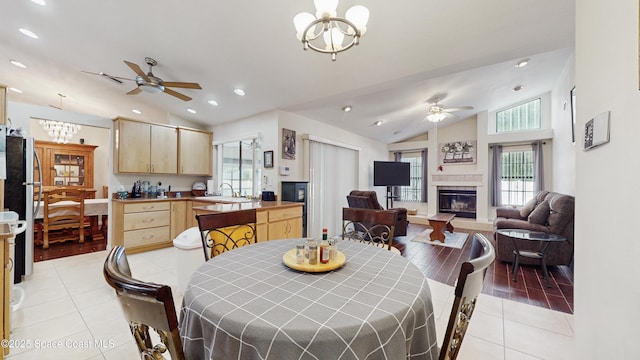 tiled dining space featuring ceiling fan with notable chandelier, lofted ceiling, and a tiled fireplace