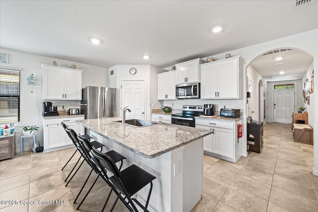 kitchen featuring sink, light stone counters, a center island with sink, white cabinets, and appliances with stainless steel finishes