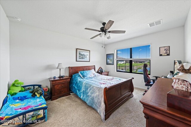 bedroom featuring ceiling fan, light colored carpet, and a textured ceiling