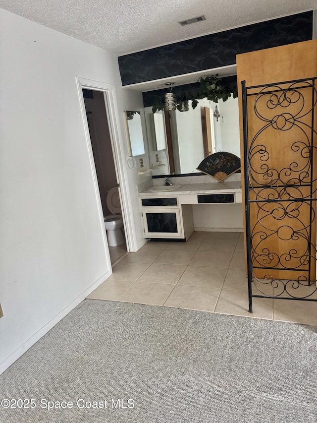 unfurnished bedroom featuring light tile patterned floors, a textured ceiling, ensuite bathroom, and sink