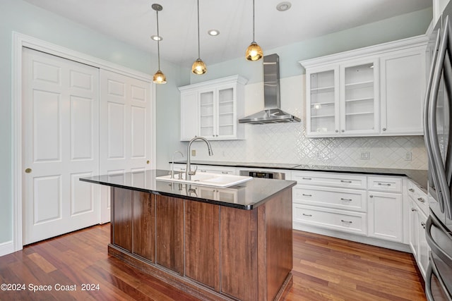 kitchen with sink, white cabinetry, hanging light fixtures, a kitchen island with sink, and wall chimney exhaust hood