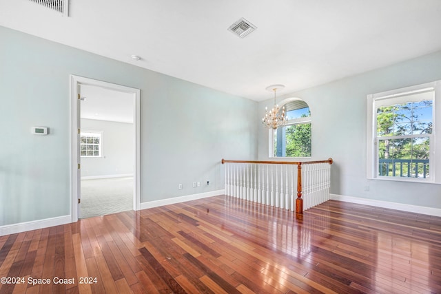 unfurnished room featuring a wealth of natural light, dark hardwood / wood-style flooring, and a chandelier