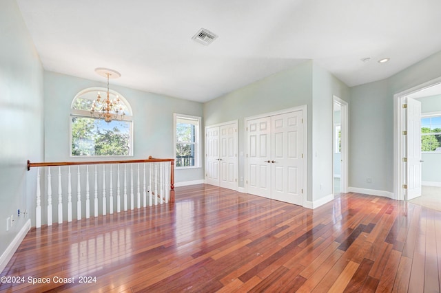 empty room featuring a healthy amount of sunlight, an inviting chandelier, and hardwood / wood-style flooring