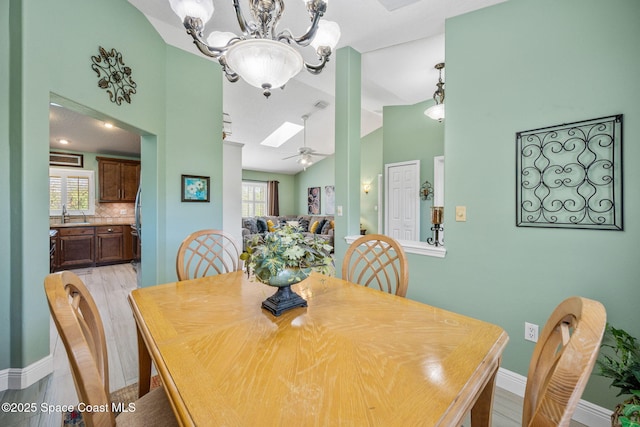 dining room featuring ceiling fan with notable chandelier, light hardwood / wood-style floors, and lofted ceiling with skylight