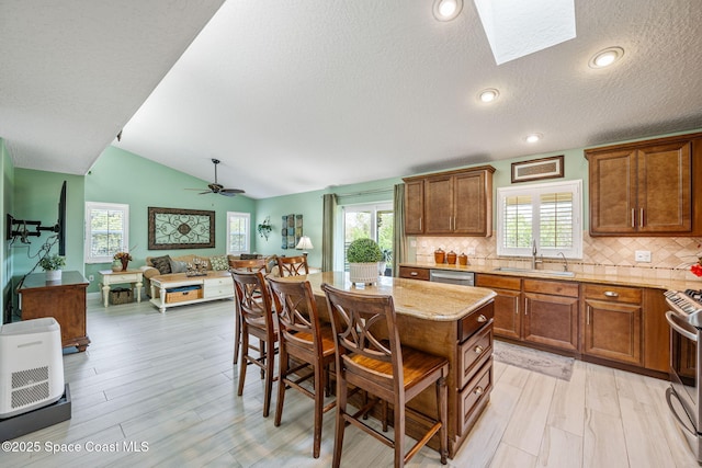 kitchen with backsplash, vaulted ceiling with skylight, ceiling fan, sink, and a center island