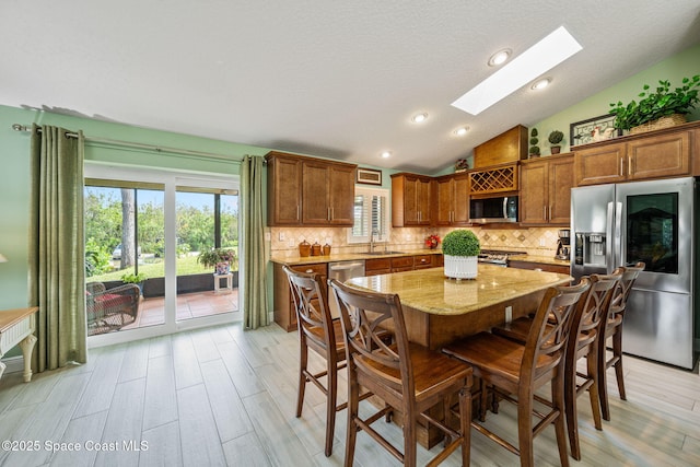 dining space with vaulted ceiling with skylight, light hardwood / wood-style floors, sink, and a wealth of natural light