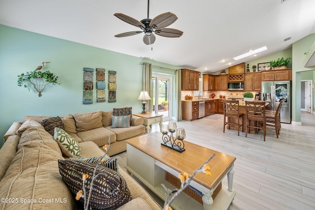 living room with ceiling fan, sink, light hardwood / wood-style floors, and vaulted ceiling