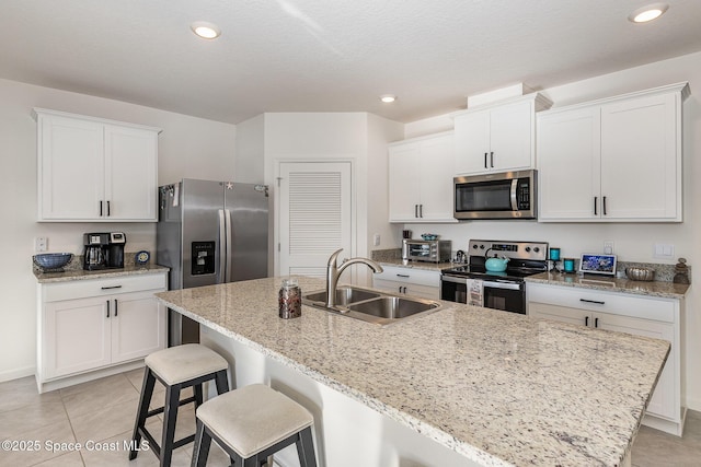 kitchen featuring stainless steel appliances, white cabinetry, a center island with sink, and sink