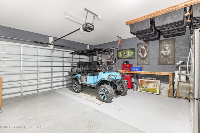 garage featuring concrete block wall, freestanding refrigerator, and a garage door opener