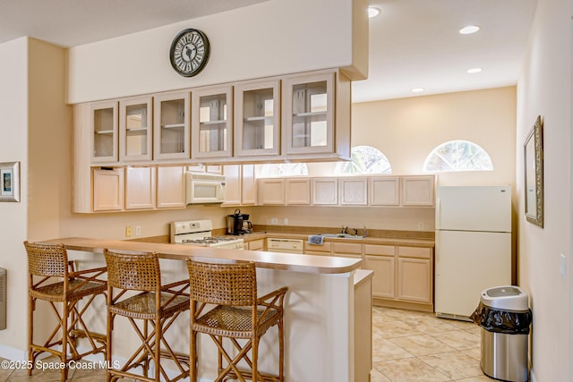 kitchen with a kitchen bar, white appliances, kitchen peninsula, and sink