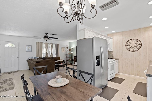 tiled dining room with ceiling fan with notable chandelier and wooden walls