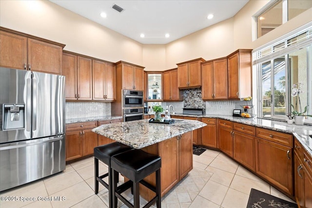 kitchen featuring a towering ceiling, light stone counters, stainless steel appliances, light tile patterned floors, and a kitchen island