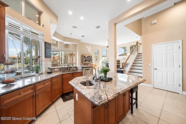 kitchen with a center island with sink, light stone counters, ceiling fan, and sink