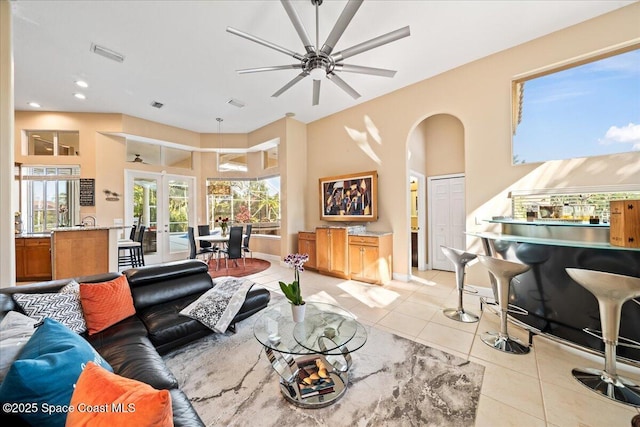 tiled living room featuring ceiling fan, a towering ceiling, and french doors