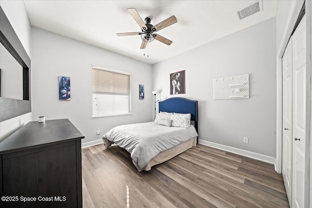 bedroom with baseboards, visible vents, ceiling fan, wood finished floors, and a closet